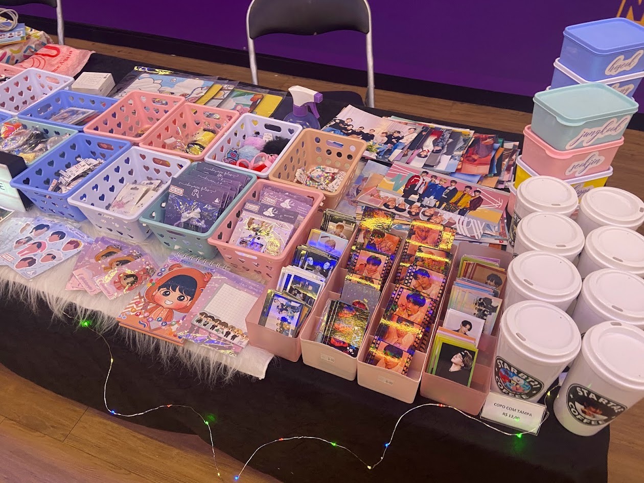Mesa e expositores da KD Store com produtos de K-pop feitos de f&atilde; para f&atilde; em evento antigo